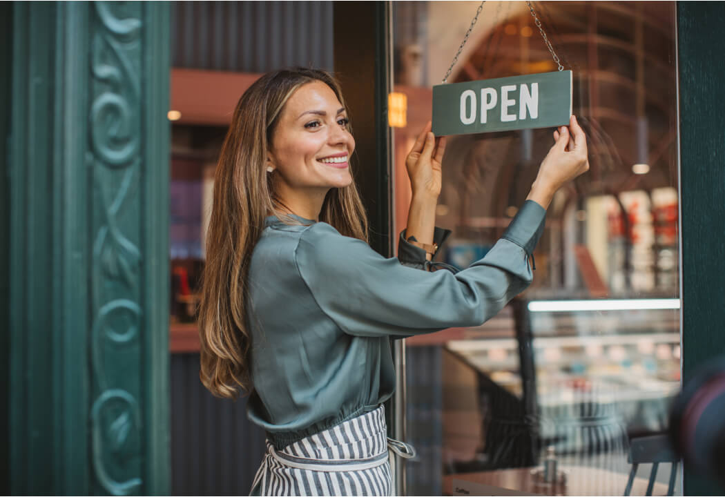 woman business owner flipping "open" sign on door